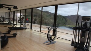 A gym with exercise equipment and a large window overlooking a lake and mountains.