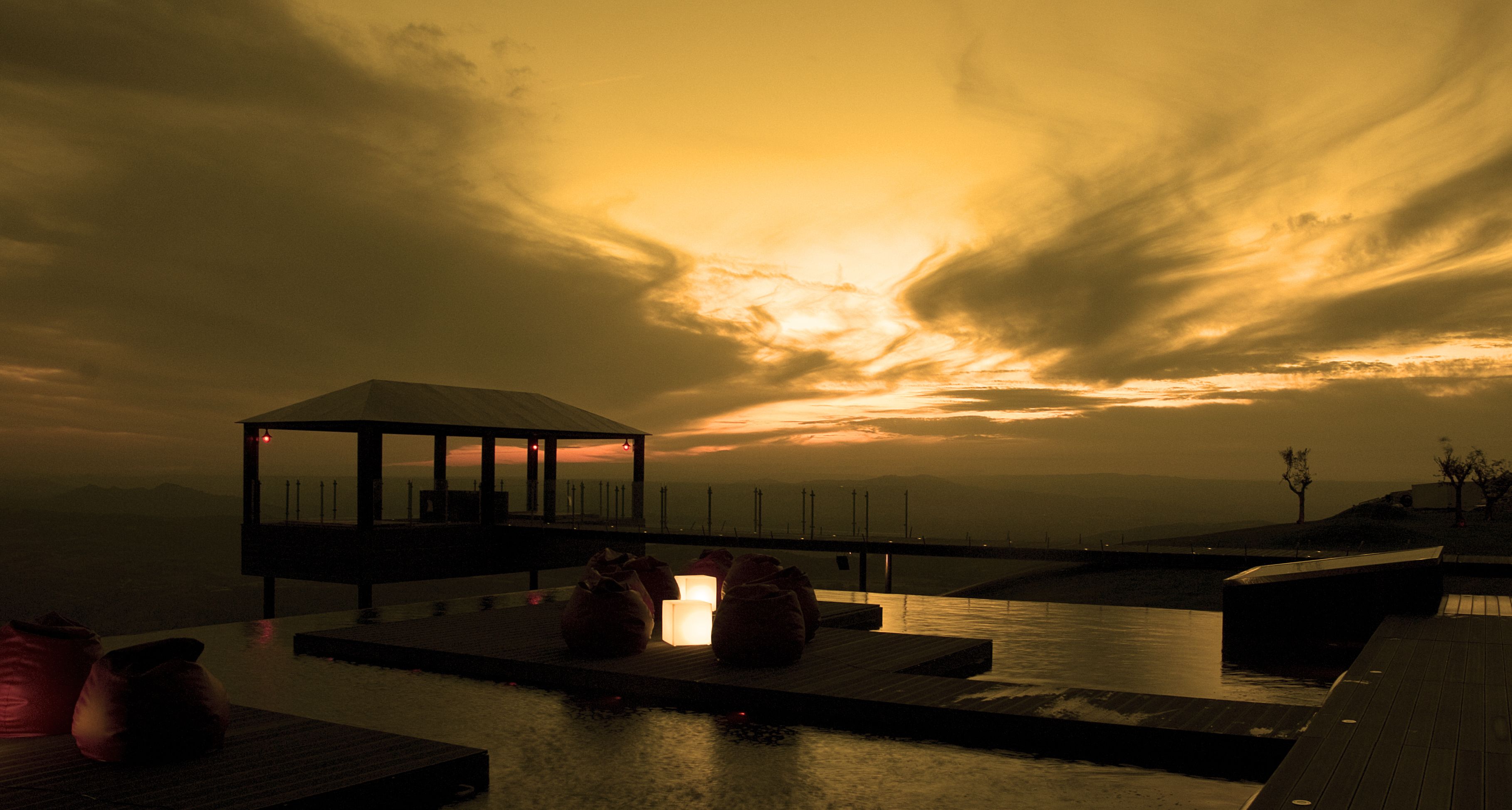 Una piscina infinita con un área de descanso cubierta por vidrio, vistas al atardecer y una superficie acuática tranquila.