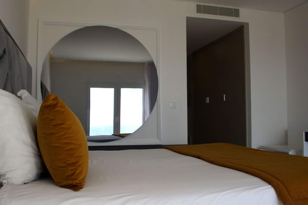 Une chambre à coucher avec un lit, un grand miroir et une vue sur l’extérieur, visible à travers une arche.
