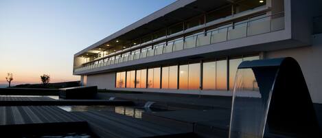 A modern building with a flat roof, large windows, and a water feature in front.