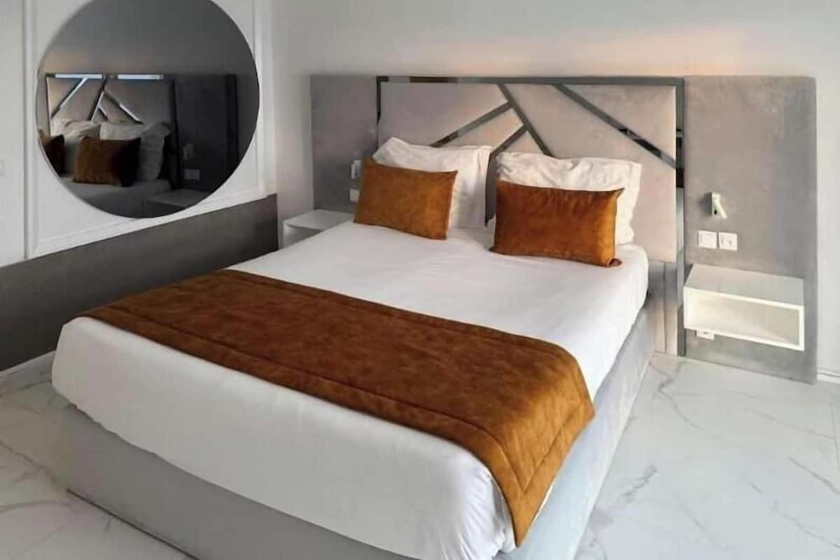 Une chambre d’hôtel moderne avec un grand lit, un miroir rond et un design minimaliste.