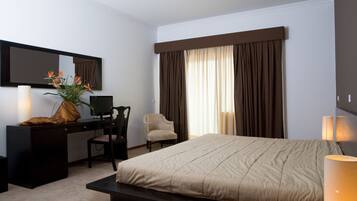 A hotel room with a bed, a desk, a chair, a desk lamp, a mirror, and a window with curtains.