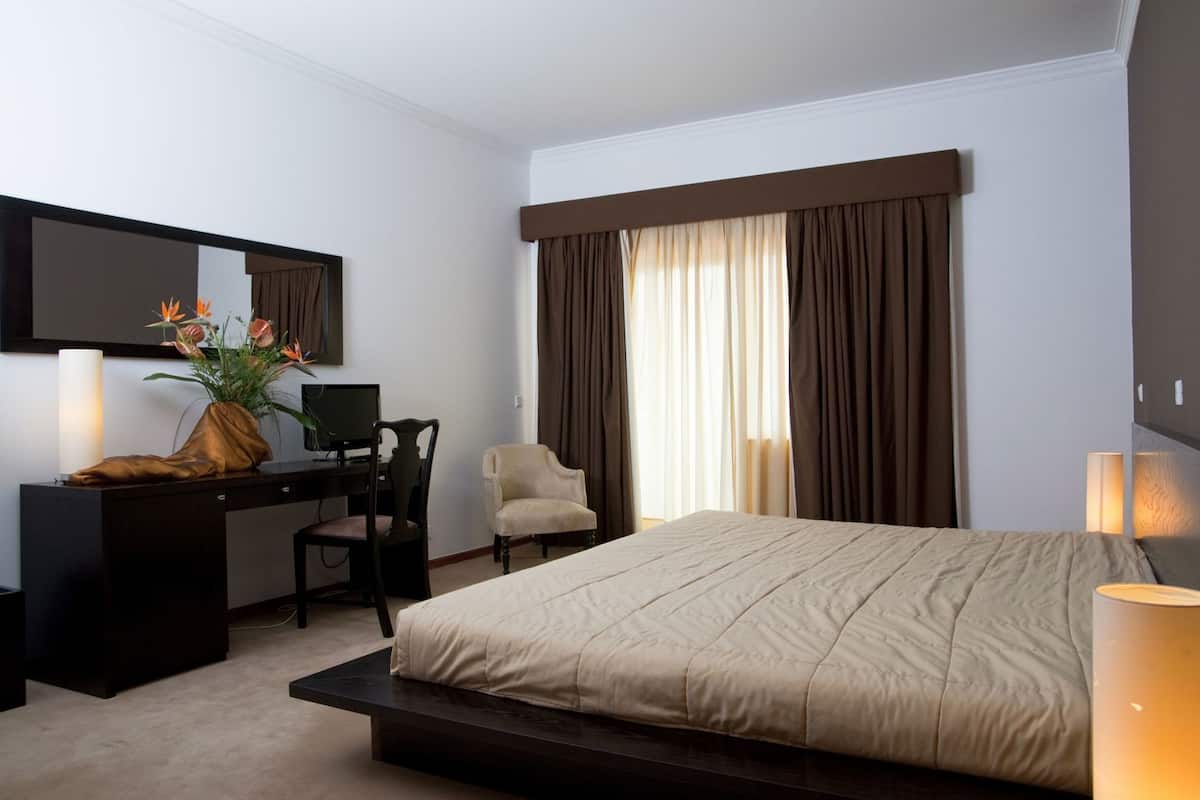 Une chambre d’hôtel avec un lit, un bureau, une chaise, une télévision et une fenêtre avec des rideaux.