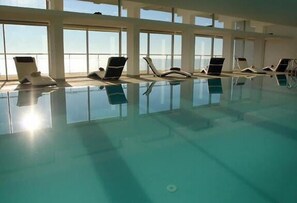 Una piscina interior con ventanas iluminadas por el sol y sillones de descanso.