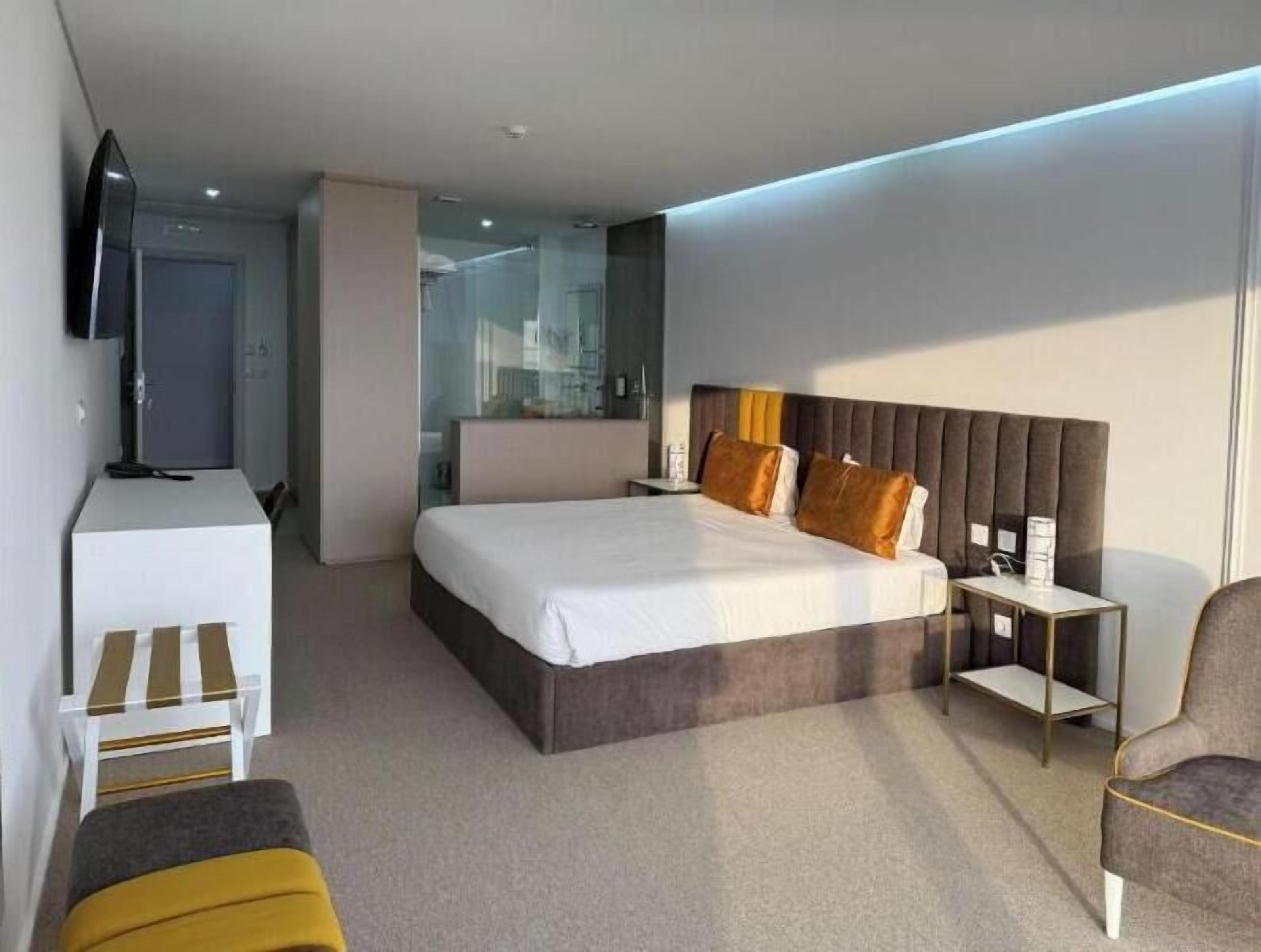 Une chambre d’hôtel moderne avec un grand lit, une table de chevet, une chaise et un téléviseur fixé au mur.