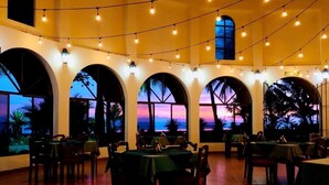 A restaurant with multiple tables and chairs, large arched windows, and string lights. - Hotel Delfin Playa Bejuco (Parrita)