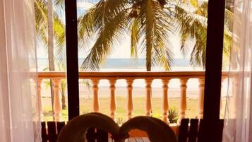 A bed with a heart-shaped towel arrangement and a view of a beach with palm trees.