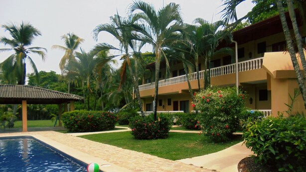 A swimming pool with beach balls, surrounded by palm trees and a building with balconies. - Hotel Delfin Playa Bejuco (Parrita)