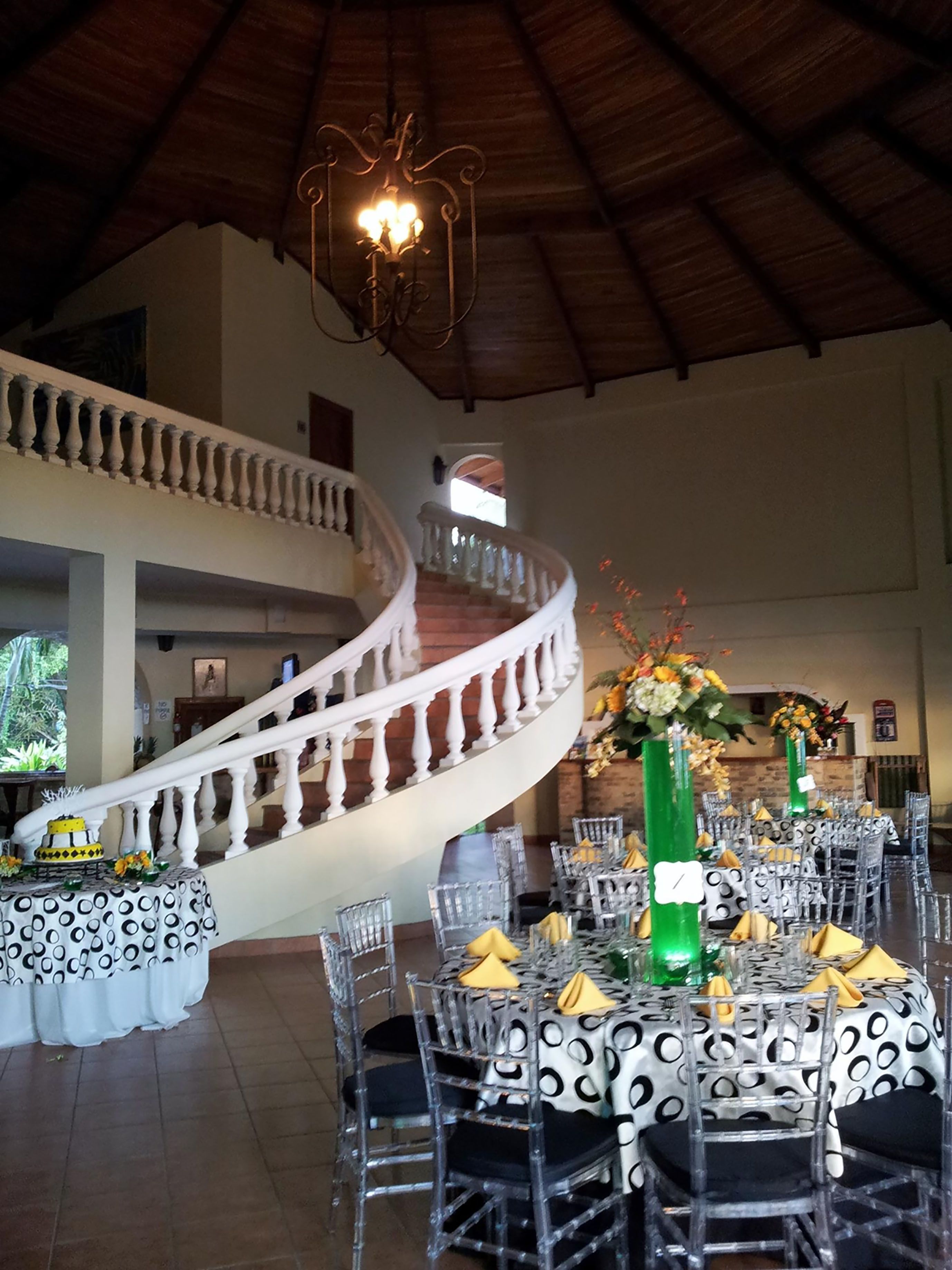 A spacious hall with a grand staircase, clear glass chairs, and tables set for a formal event.