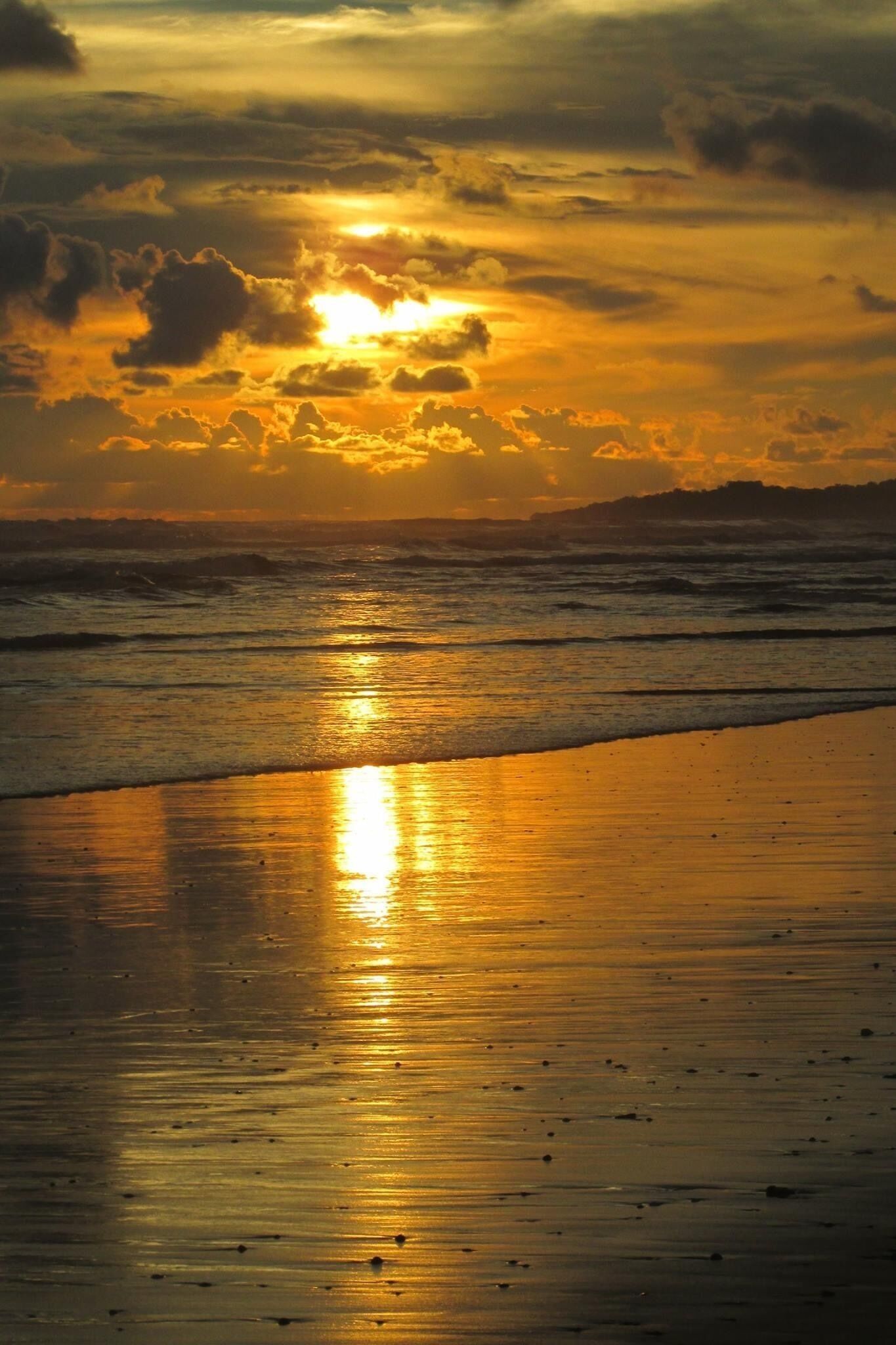 A beach at sunset with the sun reflecting off the wet sand.