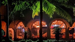A building with arched windows and a well-lit interior, surrounded by greenery. - Hotel Delfin Playa Bejuco (Parrita)