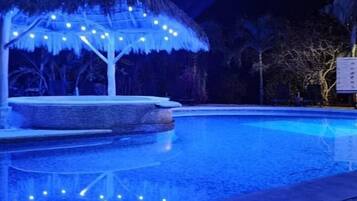 Relax by the serene pool, surrounded by a thatched-roof gazebo and string lights.