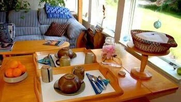 A wooden table with a tray holding tea sets, a bowl of oranges, and a basket. - Whalesong Bed and Breakfast (Homer)