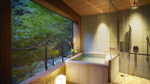 A modern bathroom with a wooden interior, a glass-enclosed shower, and a view of a forest through a large window. - Fudouguchikan (Izumisano)