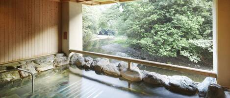 A traditional Japanese onsen with a view of a forested area through a large window.