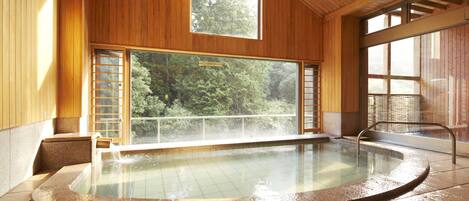 A hot tub with a view of a forest through large windows.