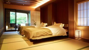 A traditional Japanese-style bedroom with tatami flooring, two beds, sliding doors leading to a balcony, and a shoji screen. - Fudouguchikan (Izumisano)