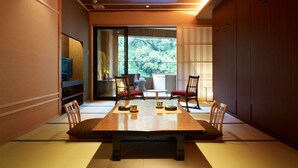A traditional Japanese-style room with tatami flooring, a low table, and sliding doors leading to a balcony with a view of greenery. - Fudouguchikan (Izumisano)