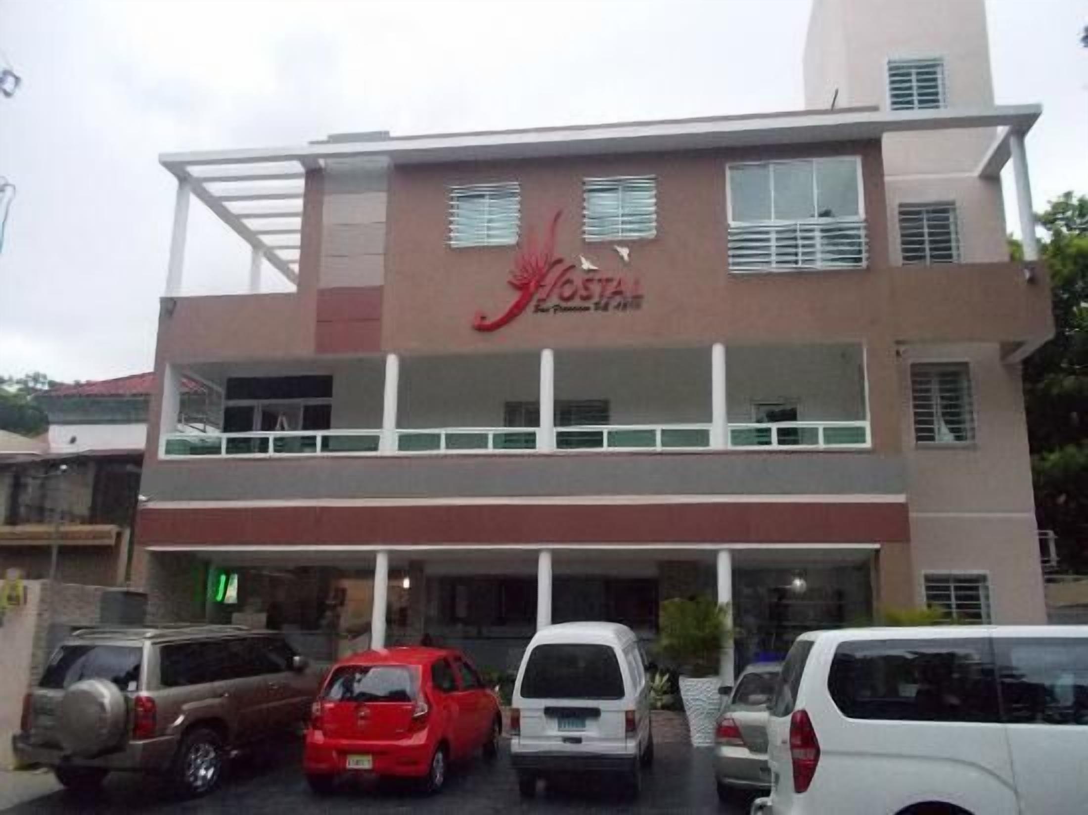 A two-story building with a sign reading "Hostal". There are several parked cars in front.