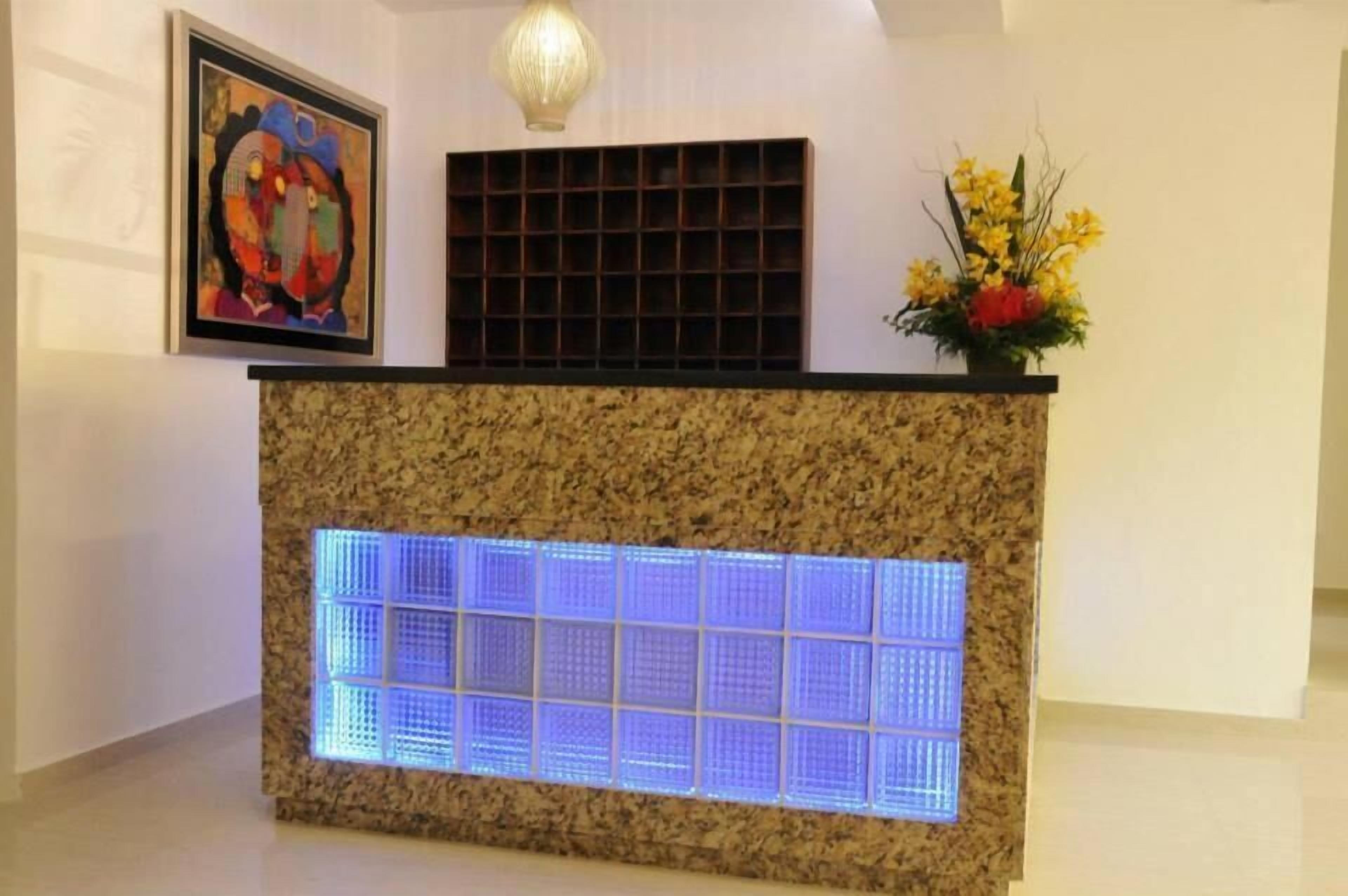 A reception desk with a granite top, a blue illuminated panel, a framed artwork, a decorative light fixture, and a floral arrangement.