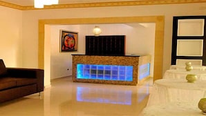 Un hall d’hôtel avec un canapé marron, un comptoir de réception éclairé en bleu et un mur décoratif orné d’un tableau encadré.