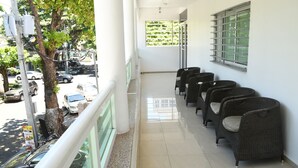 Un balcon avec des fauteuils en osier, un sol carrelé et une vue sur les voitures garées et les arbres.