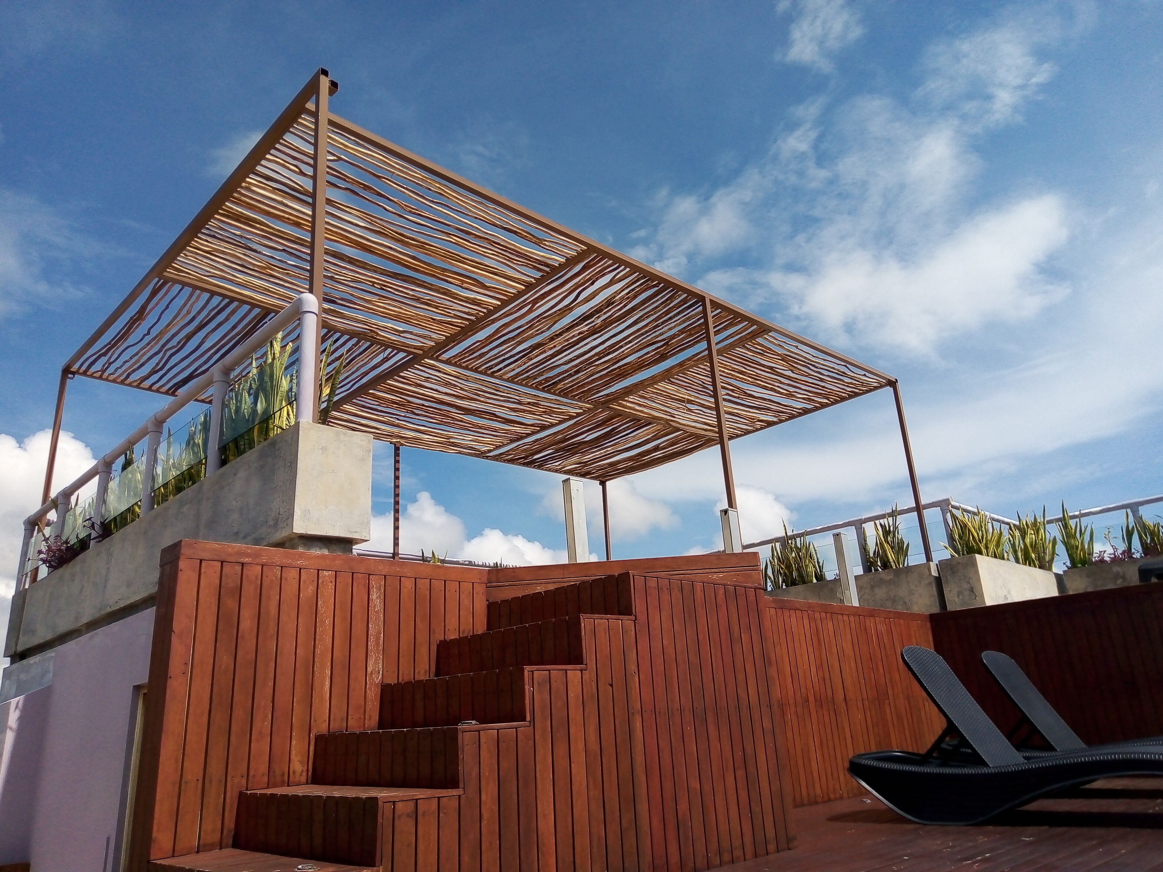 A modern outdoor area with a wooden pergola, a set of wooden stairs, and a black lounge chair.