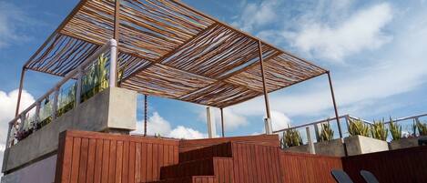 A modern outdoor area with a wooden pergola, a set of wooden stairs, and a black lounge chair.