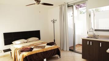 A bedroom with a bed, a ceiling fan, a coat rack, a bathroom with a sink, and a sliding glass door to a balcony.