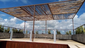 A covered outdoor area with a wooden floor and metal beams, surrounded by plants and a view of the sky. - IRIS Studios & Apartments (Playa del Carmen)