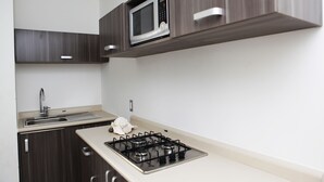 A modern kitchen with a built-in microwave, a gas stove, a sink, and wooden cabinets. - IRIS Studios & Apartments (Playa del Carmen)