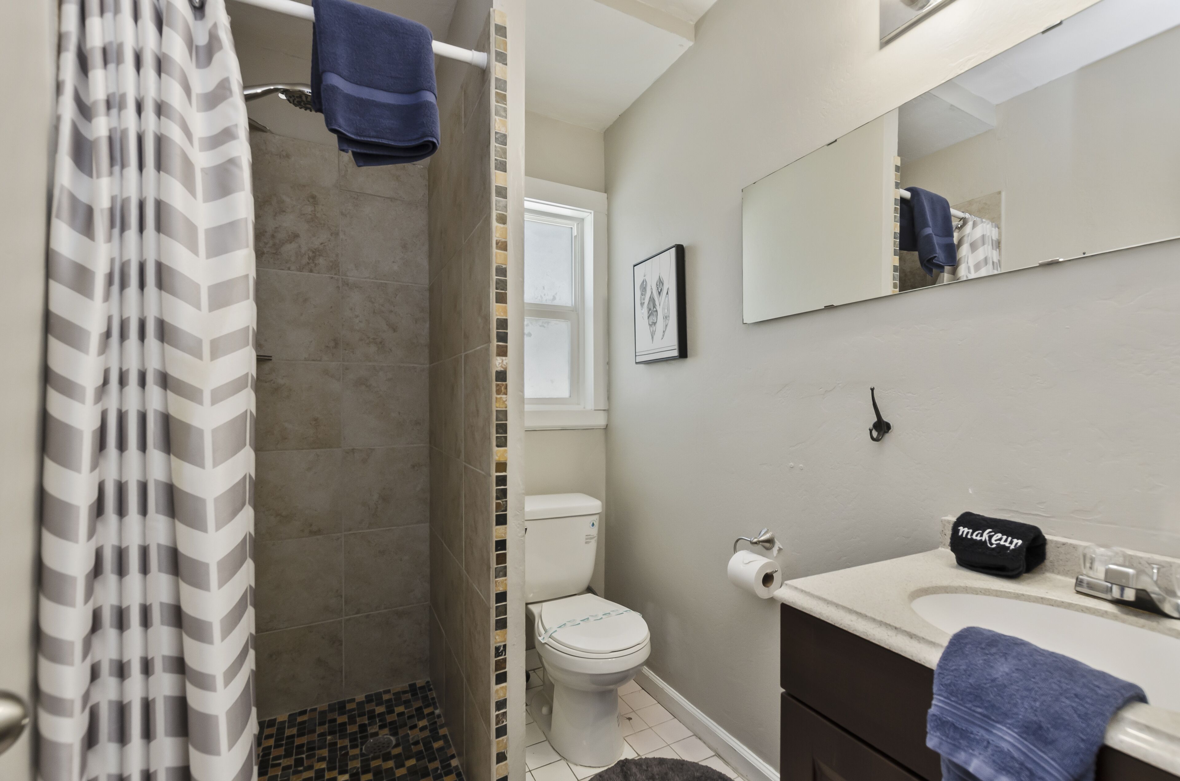 A bathroom with a shower, toilet, sink, and a mirror.