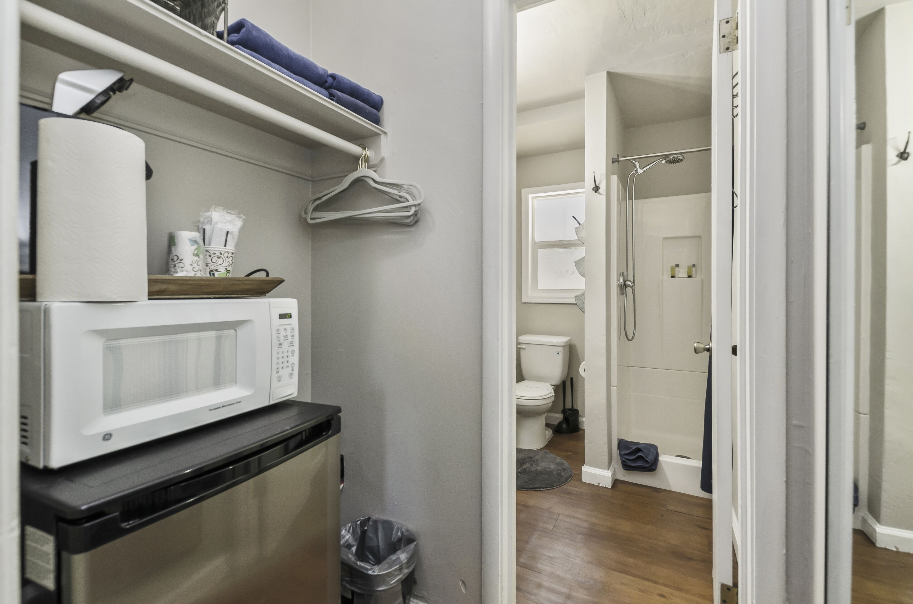 Una kitchenette compacta con microondas, un pequeño cubo de basura y un perchero.