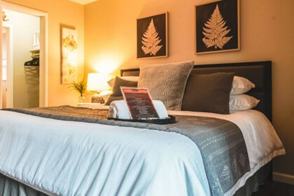 A neatly made bed with a light blue bedspread and pillows, a bedside table with a lamp, and two wall-mounted leaf decorations.