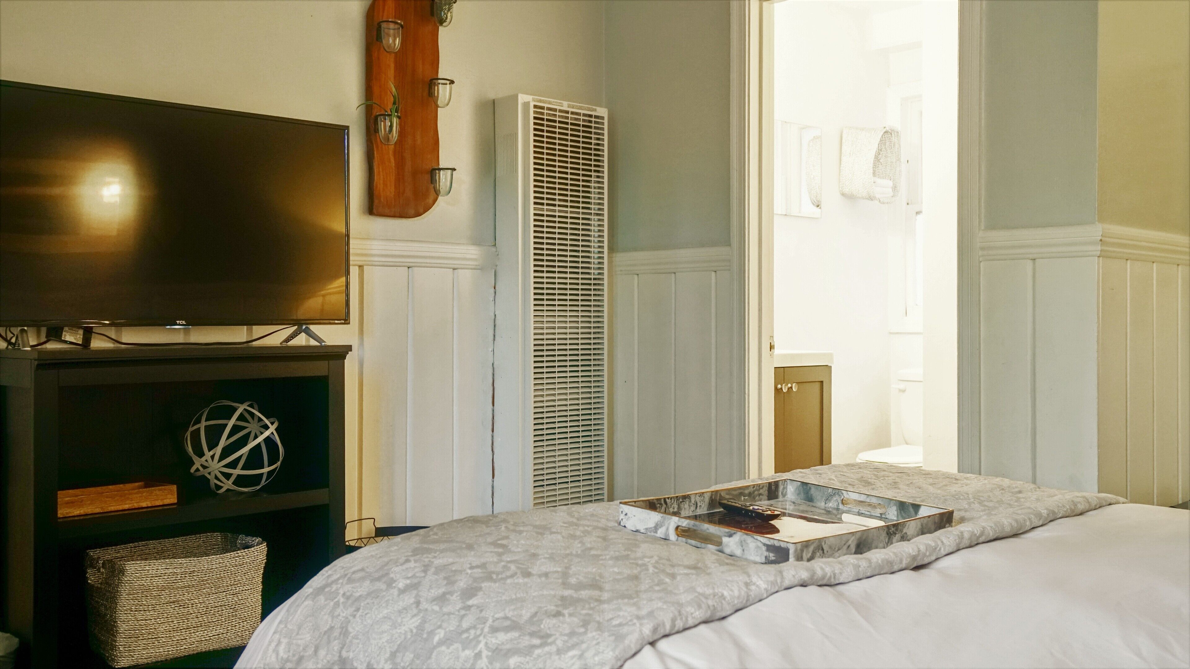 Ein Schlafzimmer mit einem Bett, einem Fernseher, einem Heizkörper und einer Tür zu einem Badezimmer.