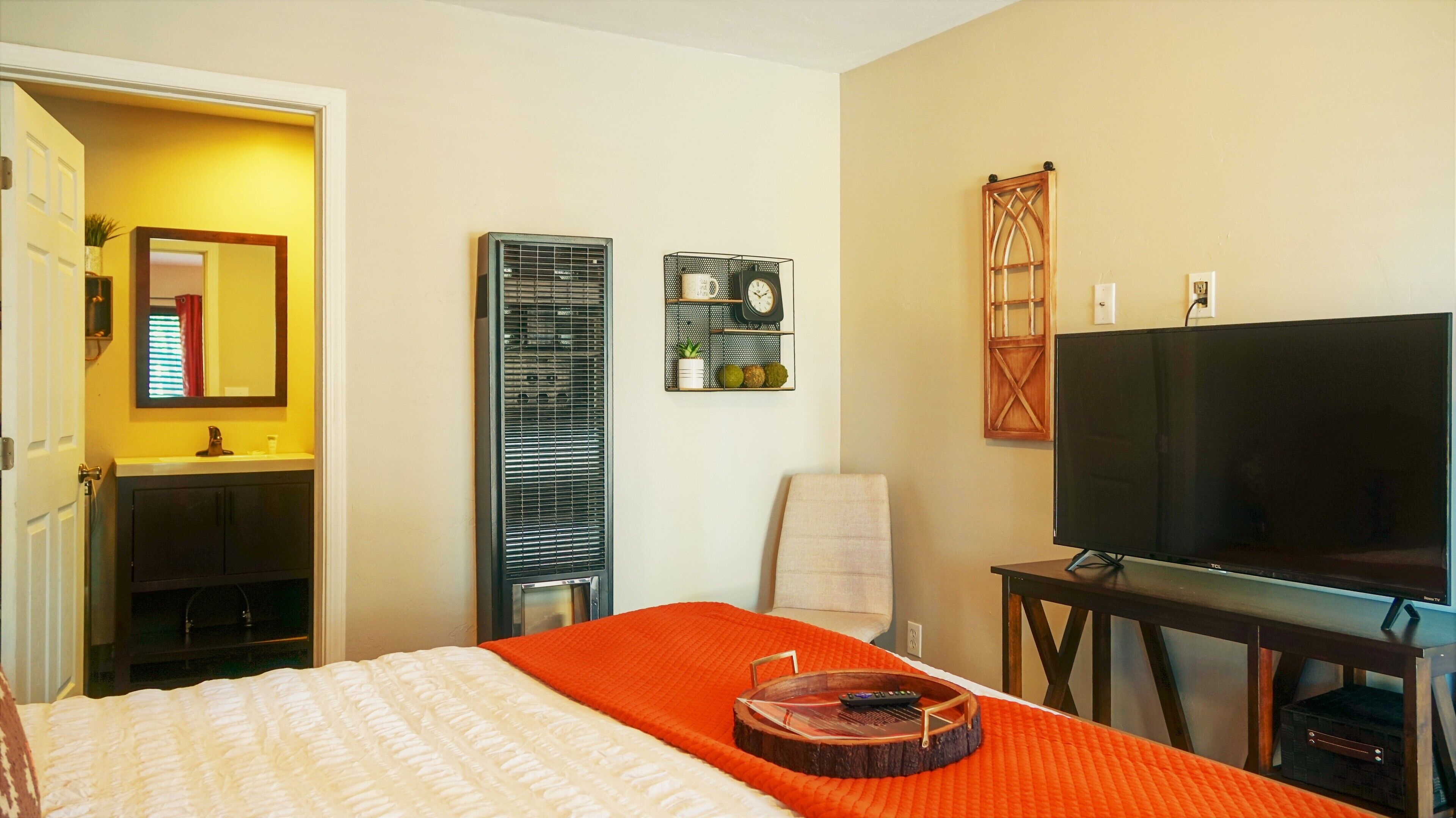 Habitación de hotel con cama, televisor, calefacción, espejo y estante con un reloj y objetos decorativos.