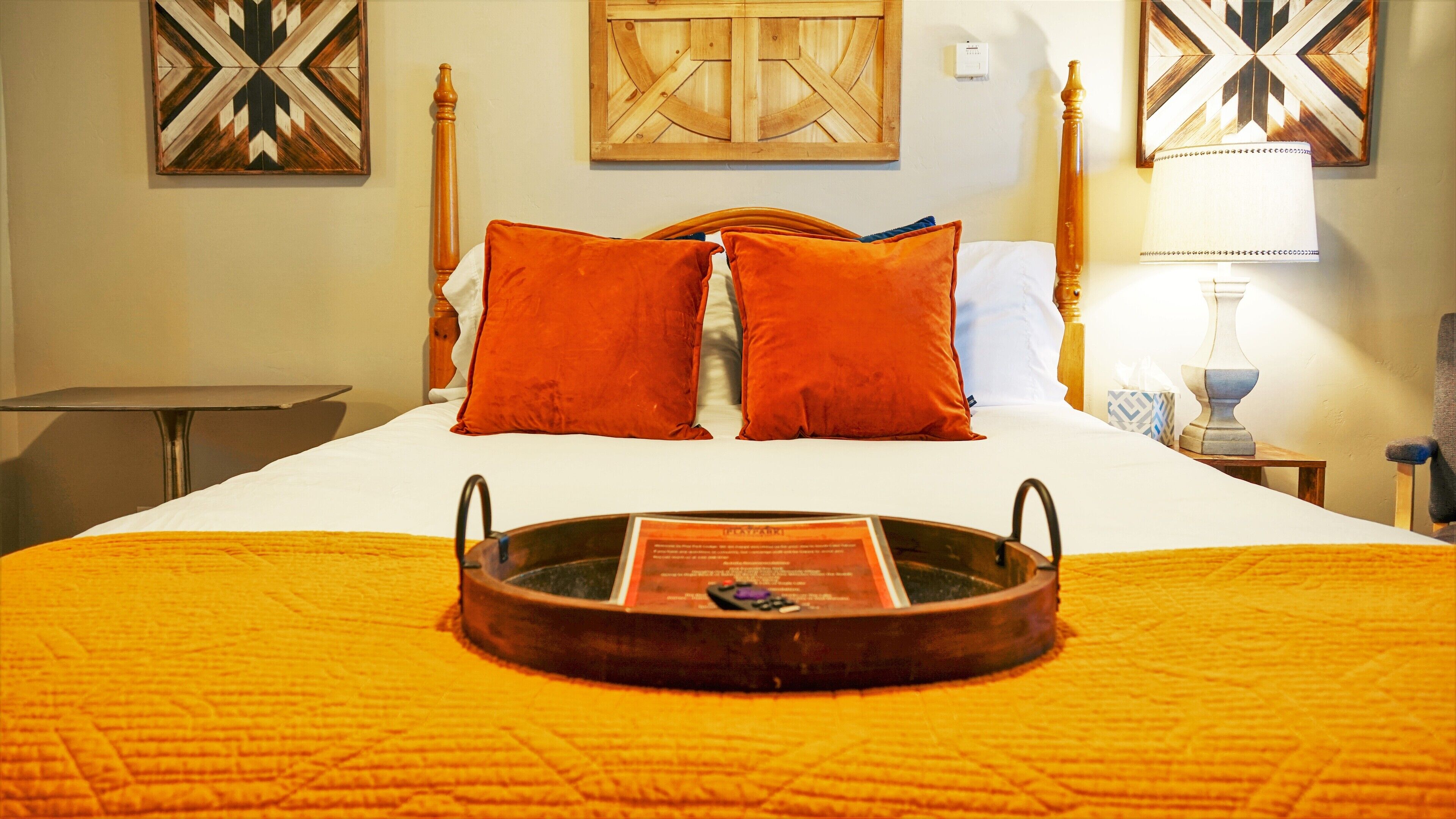 Una cama bien hecha con una bandeja, dos almohadas anaranjadas y un cabecero de madera.