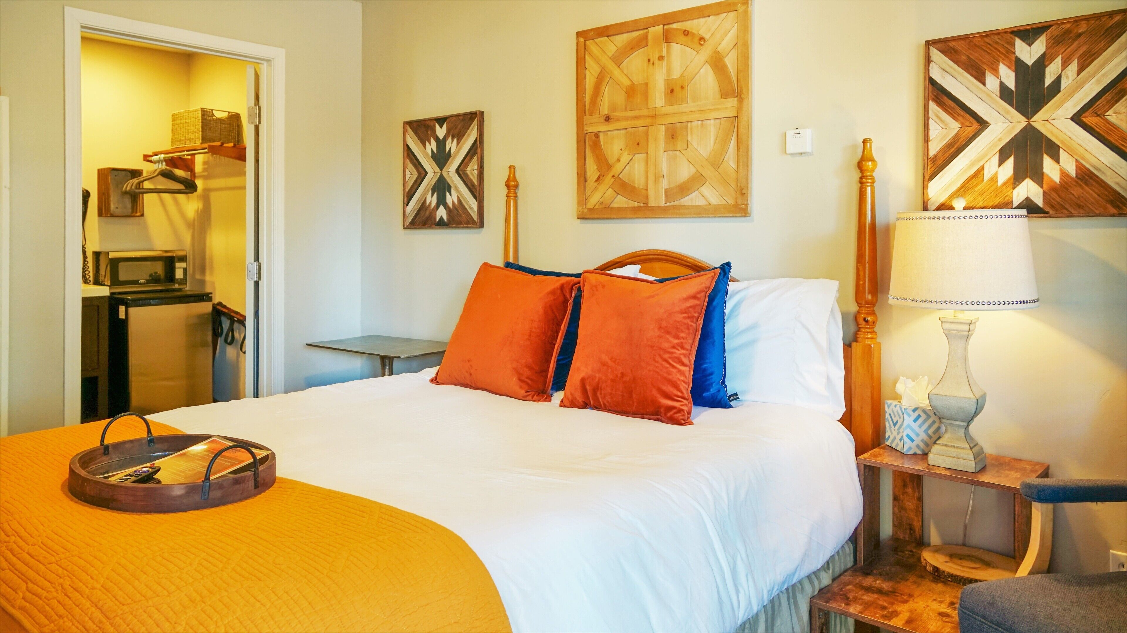 Quarto de hotel com uma cama, mesa de cabeceira com luminária, painel de cabeceira em madeira e obras de arte nas paredes.