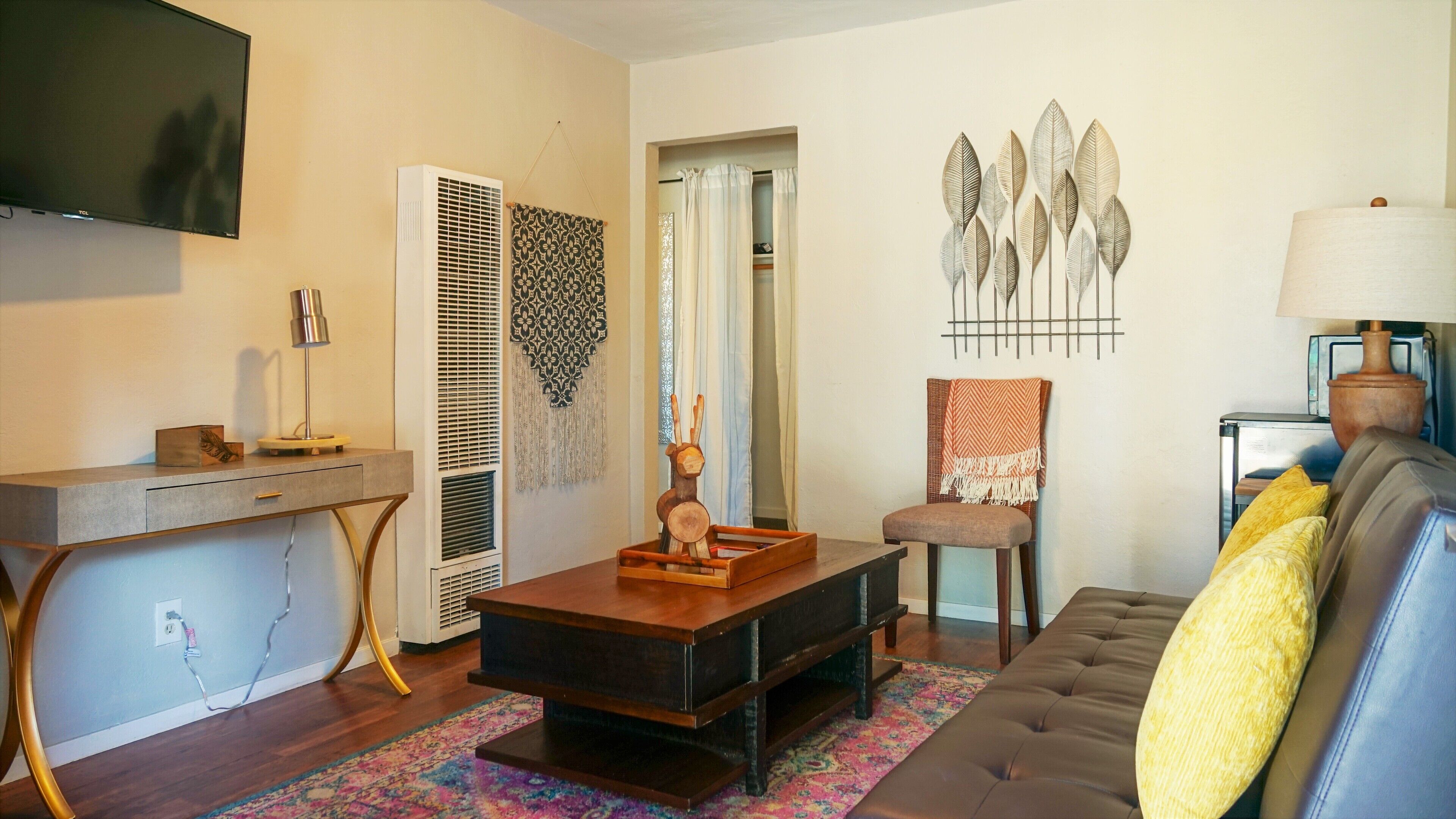 A living room with a flat-screen TV, a wooden coffee table, a sofa, a chair, and a decorative wall piece.