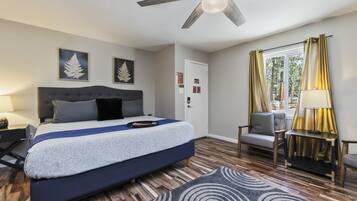 Un dormitorio moderno con una cama grande, un ventilador de techo, una ventana con cortinas y una mesita de noche con lámpara.
