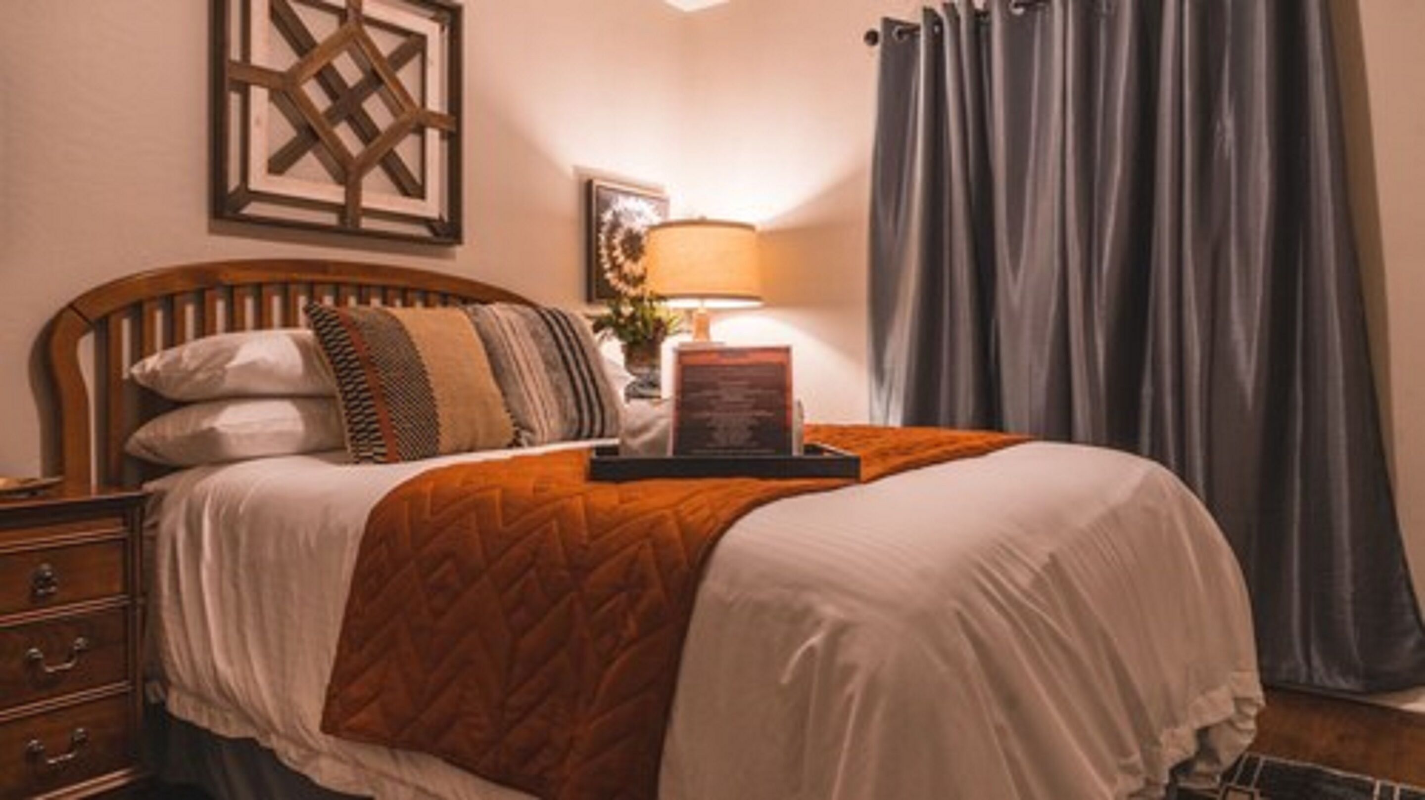 A neatly made bed with a wooden headboard, a bedside table with a lamp, and a framed picture on the wall.