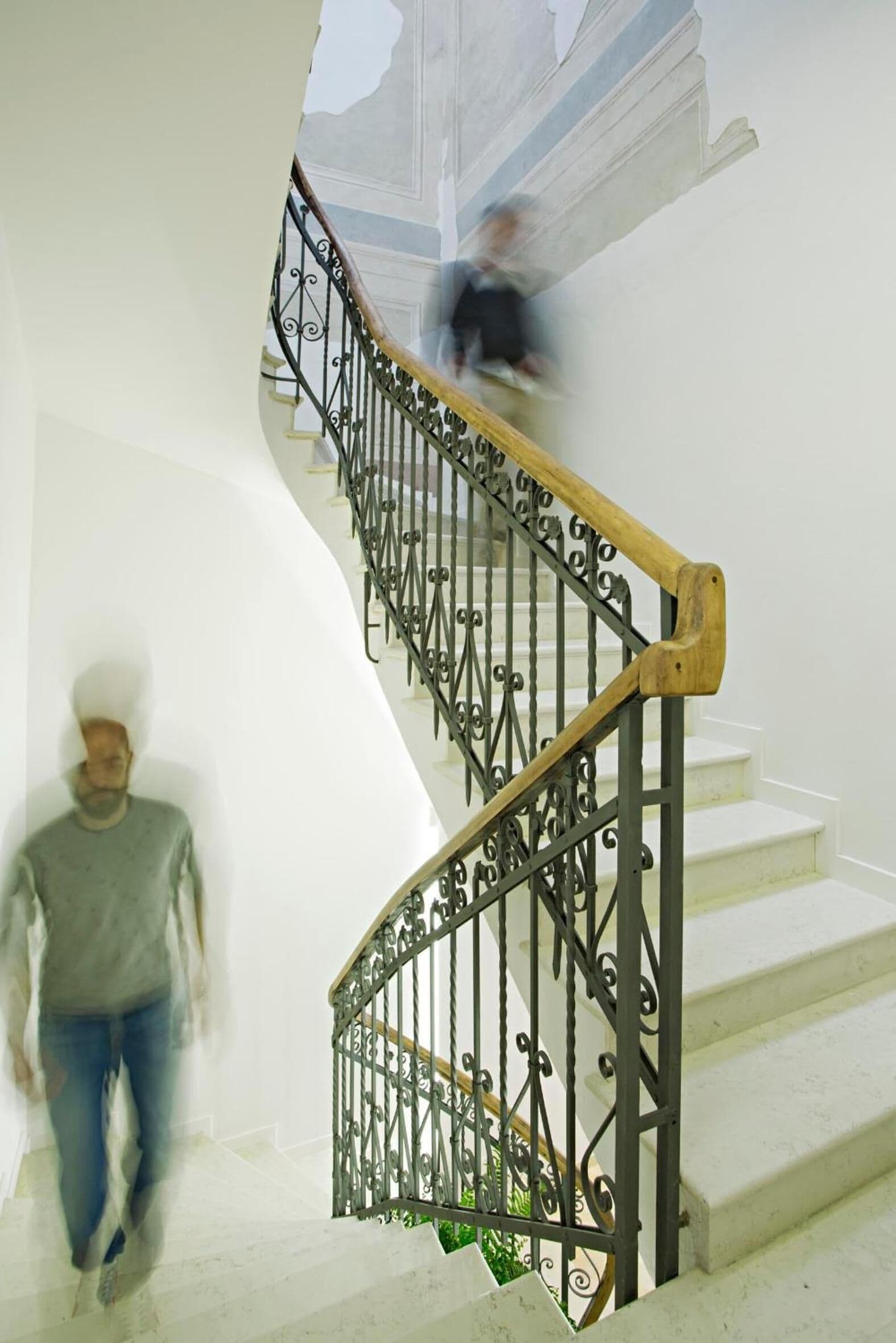 Una scala con ringhiere in metallo decorate e un corrimano in legno, che conduce a un piano superiore.