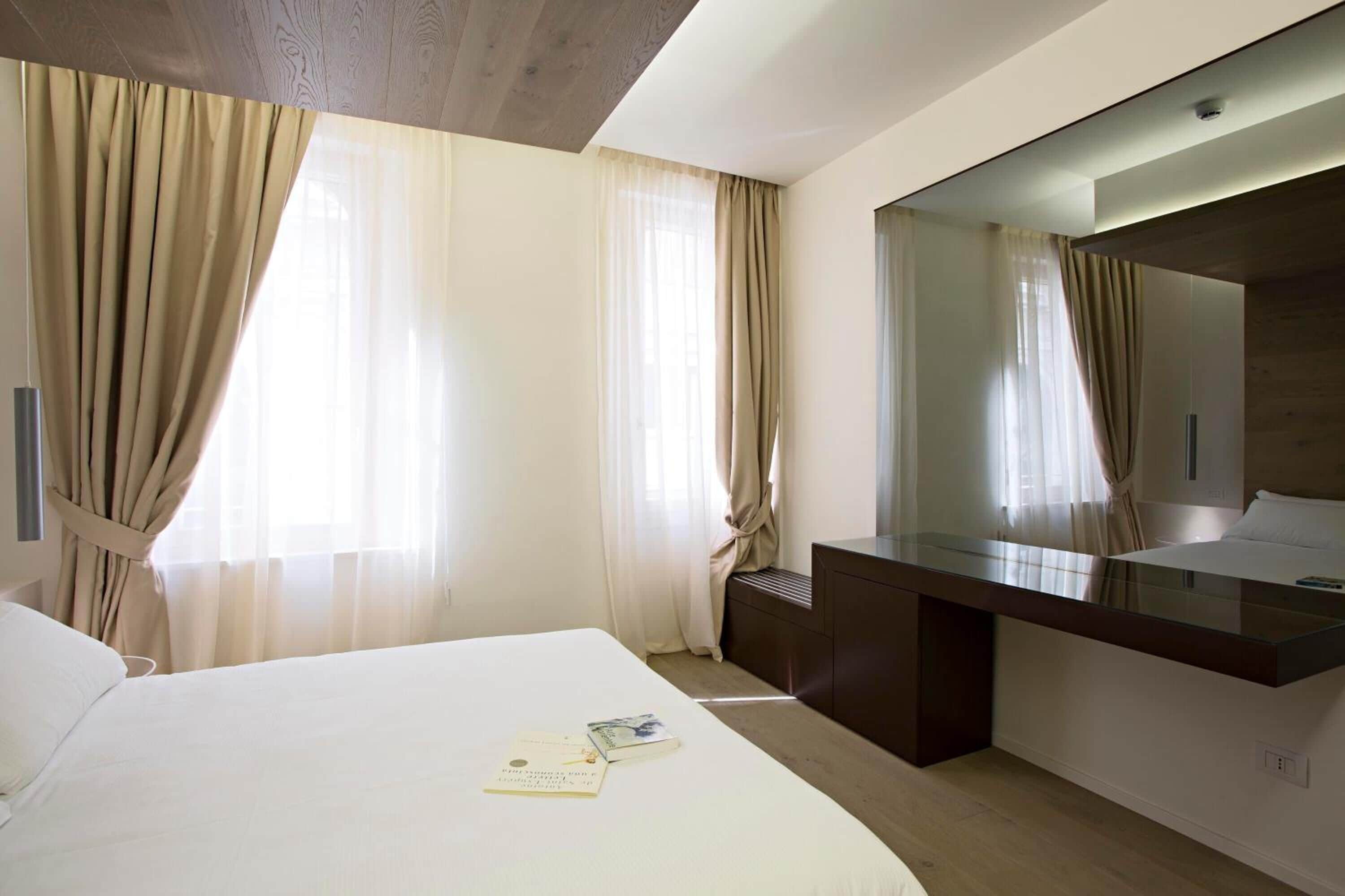 Una habitación de hotel con una cama grande, una mesita de noche, un espejo y una ventana con cortinas.