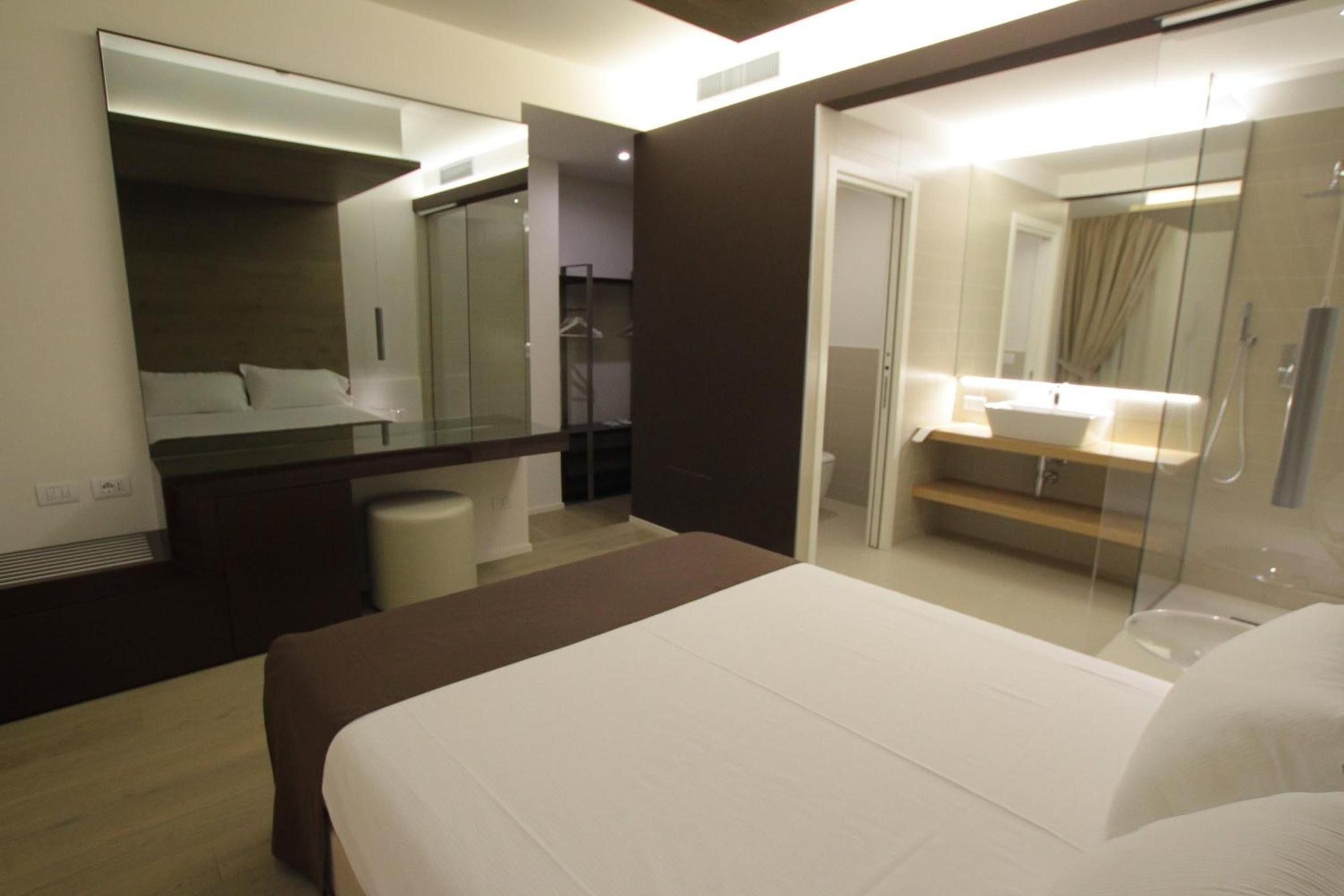 A modern hotel room with a large bed, a separate bathroom with a glass shower enclosure, and a walk-in closet.