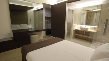 A modern hotel room with a large bed, a separate bathroom with a glass shower enclosure, and a walk-in closet.