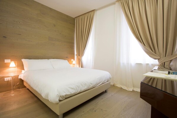 A bedroom with a wooden wall, a bed, a nightstand with a lamp, and a dresser. - Borgoleoni 18 (Ferrara)