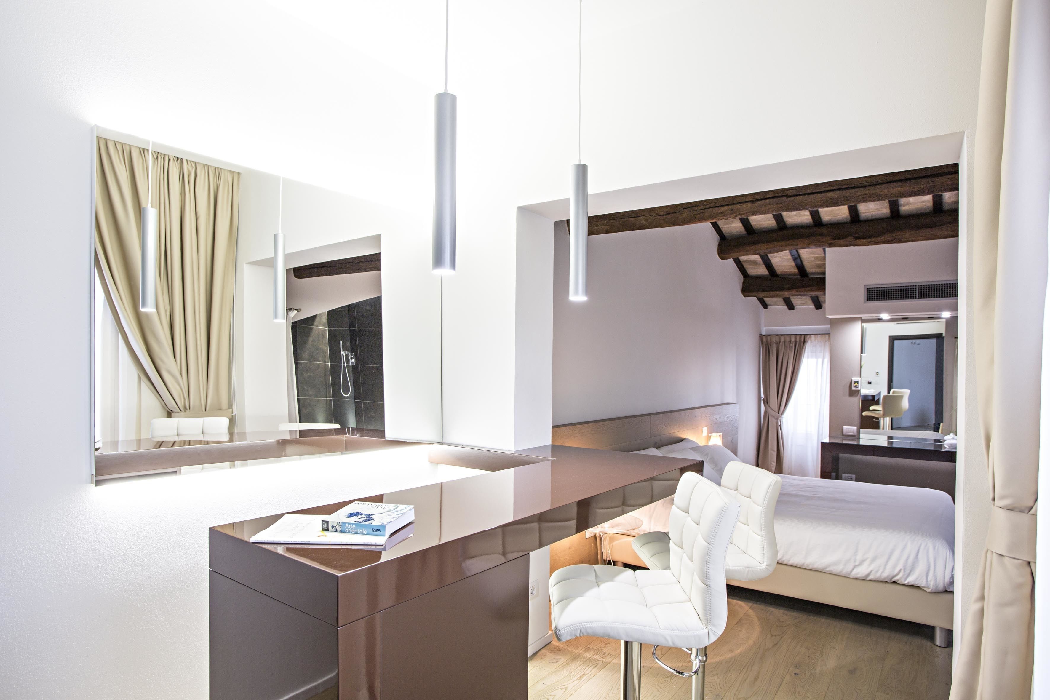 A modern hotel room with a large bed, a desk with a chair, a mirror, and a window with curtains.
