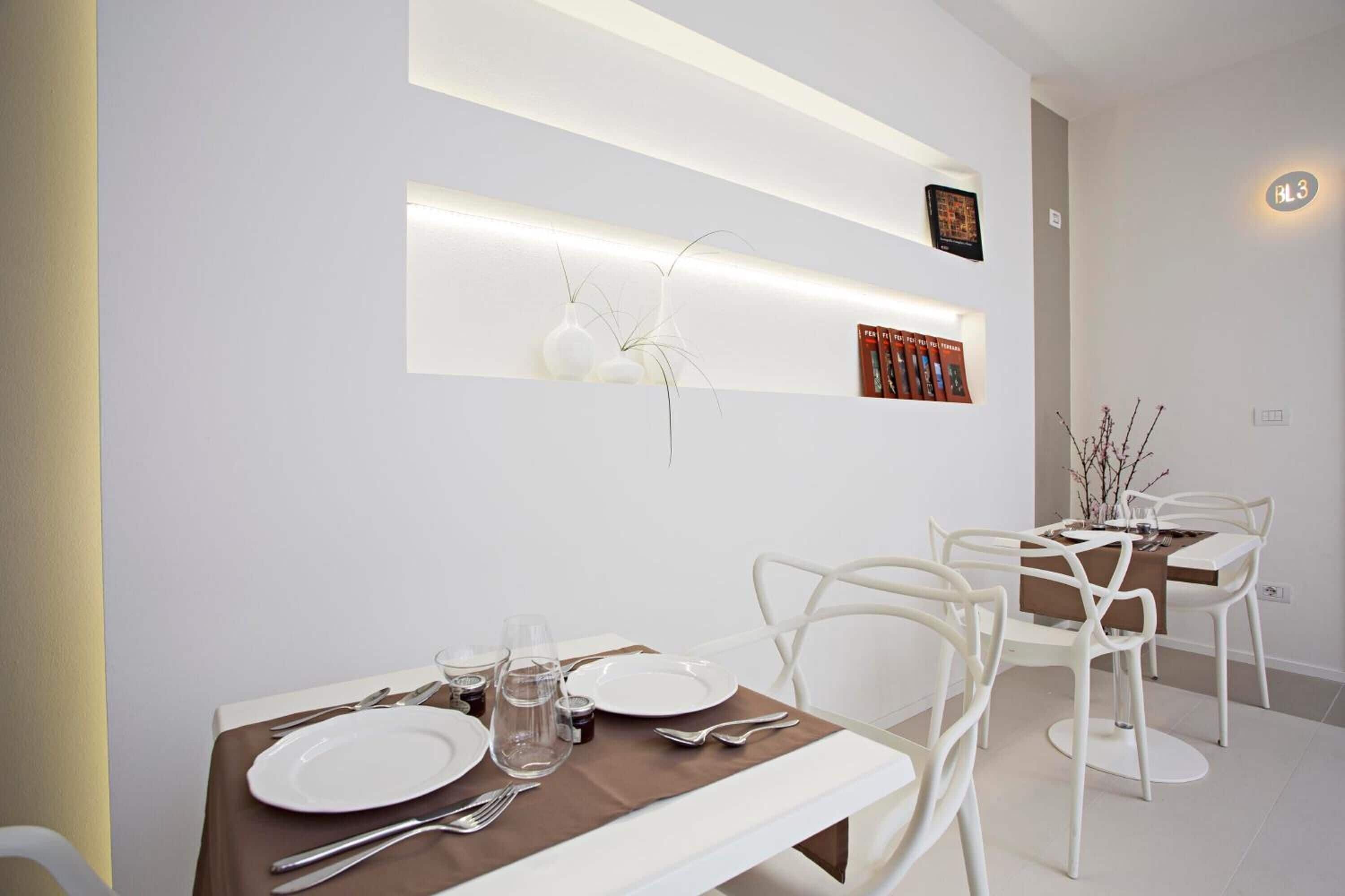 A modern dining area with a white table set for four, white chairs, and a wall-mounted shelf with decorative items.