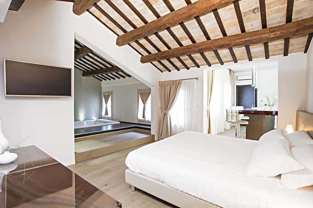 A modern bedroom with a large bed, a flat-screen TV, and a wooden ceiling.