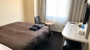 A hotel room with a bed, a desk, a chair, a small round table, a television, and a window with curtains.